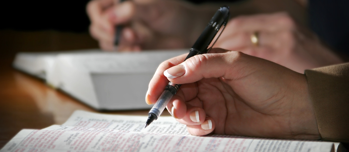 2 people's hands sitting and writing notes in Bible